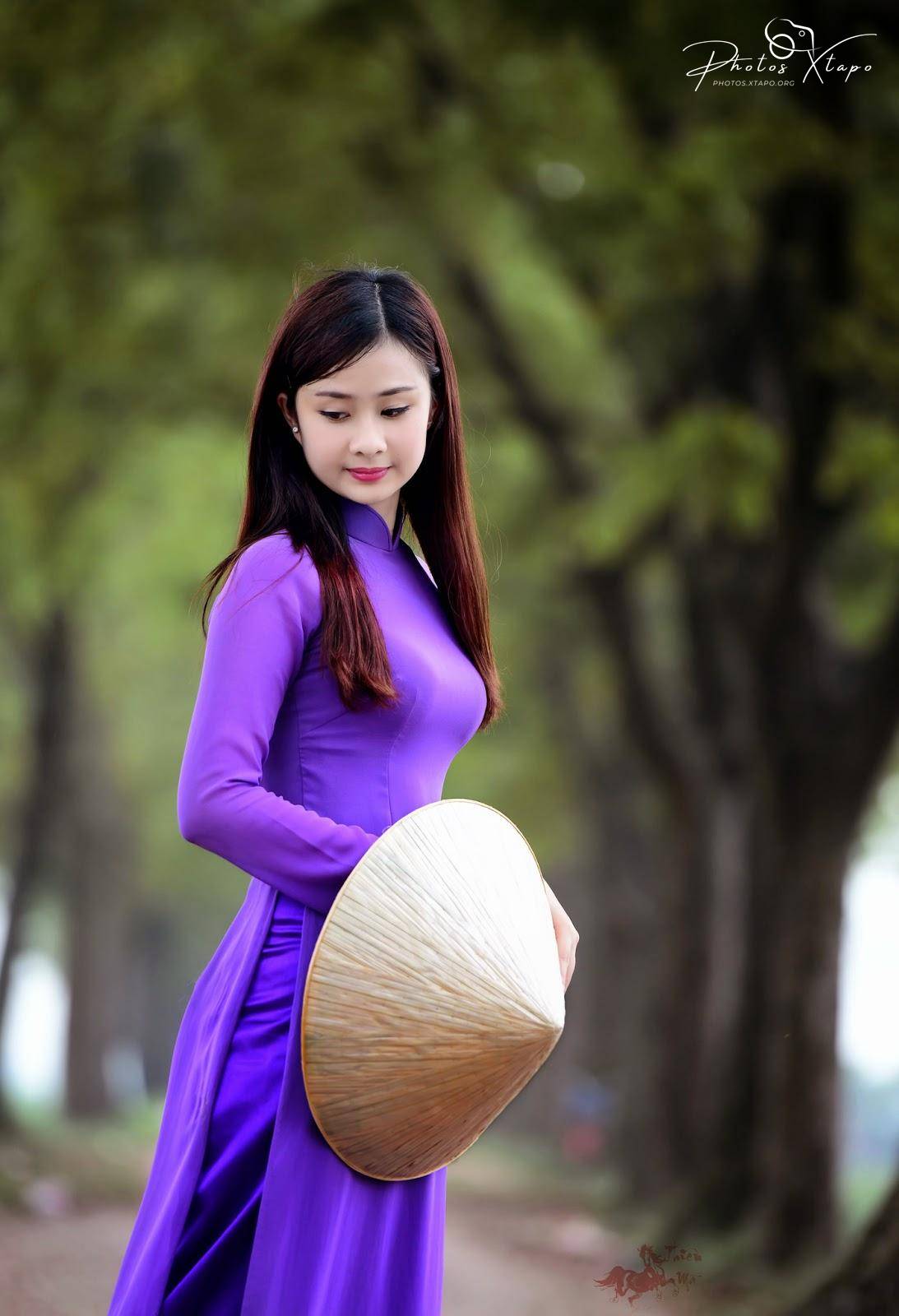 A young woman in a traditional Vietnamese Ao Dai dress holds a Non La (conical hat) in a park setting.