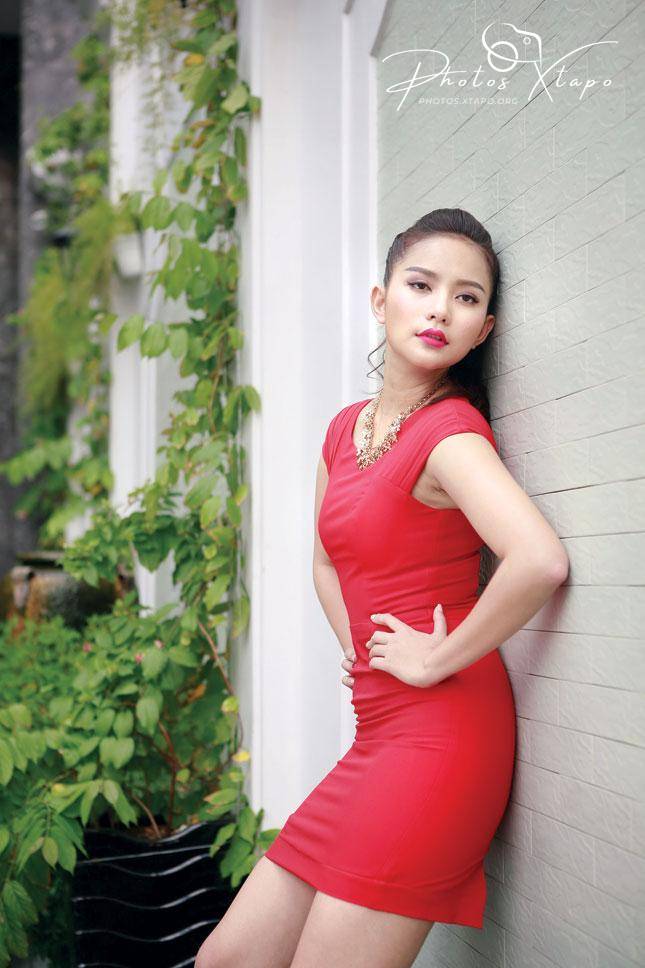 A young woman in a red dress poses against a wall.