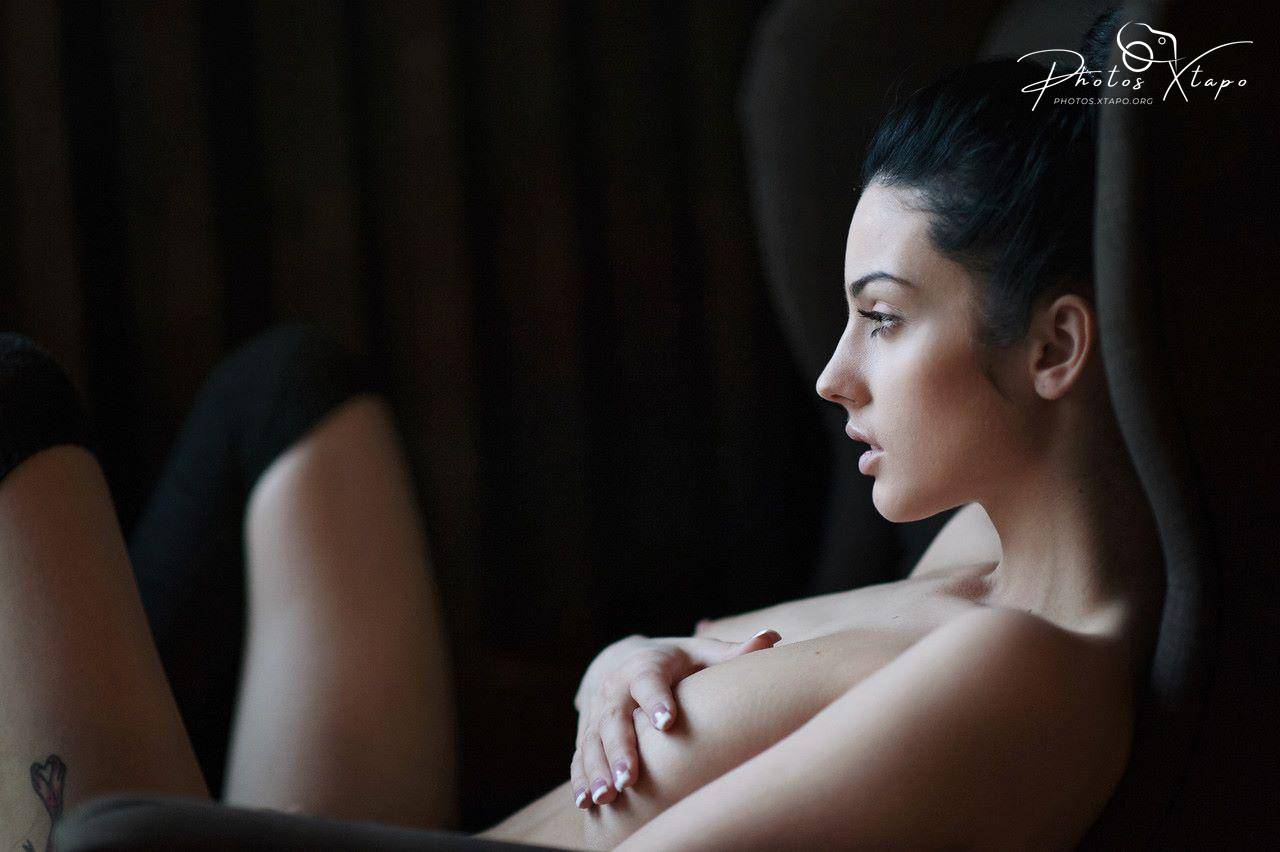 A woman sits in a dimly lit room, her expression thoughtful and pensive.