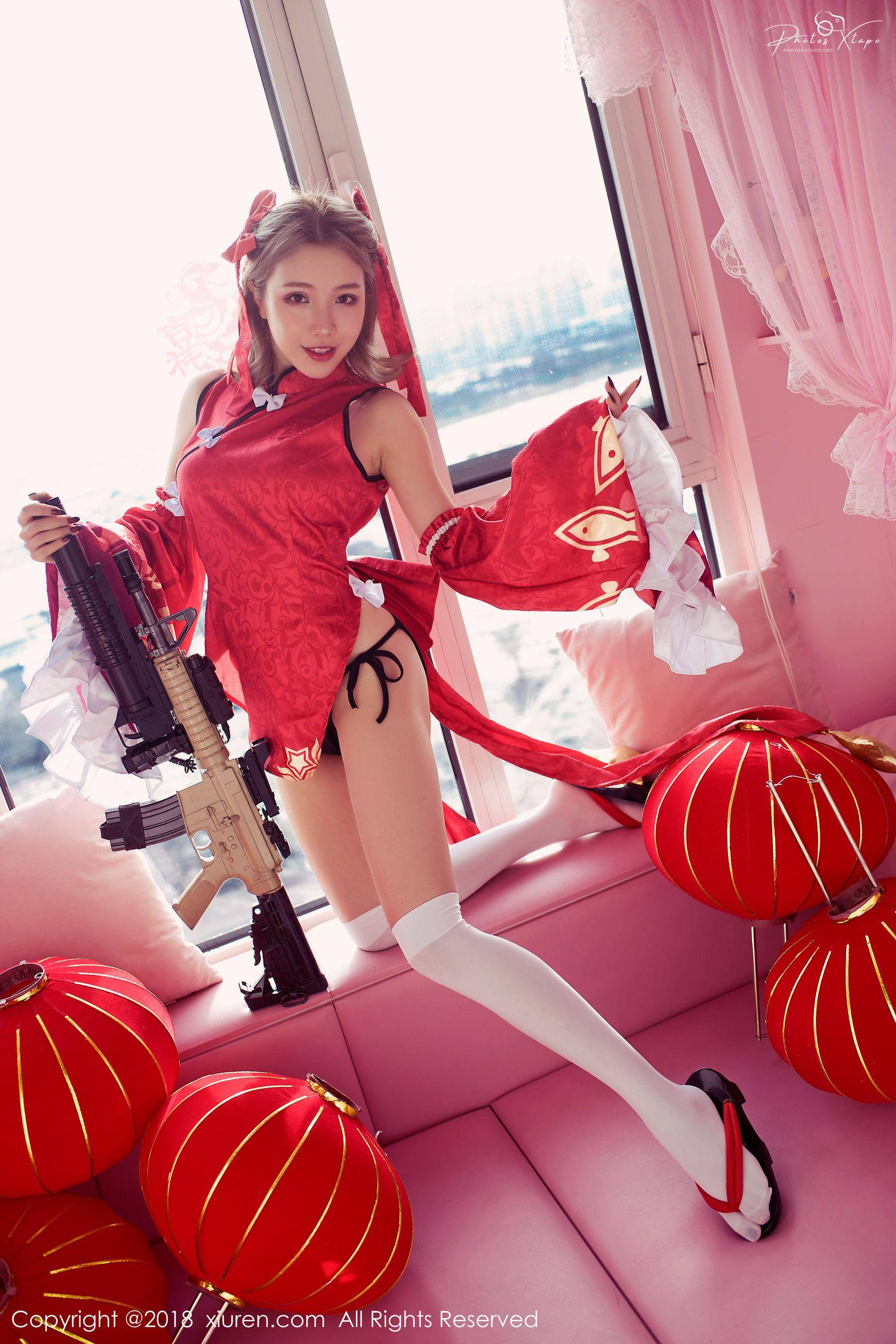 A young woman in a vibrant red Chinese-style dress and white thigh-high socks poses with a rifle.  She is surrounded by red Chinese lanterns in a pink room.