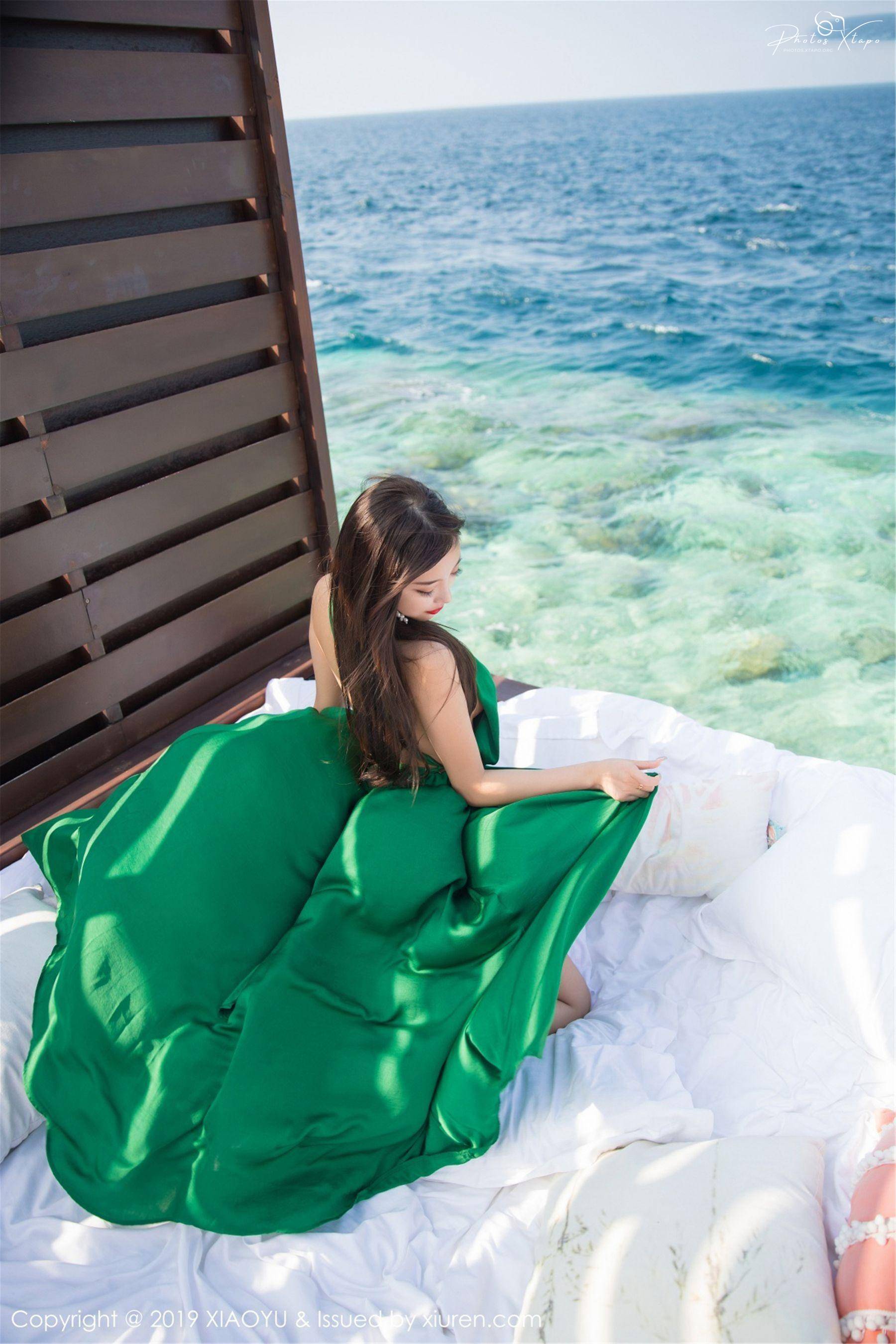 A woman in a vibrant green dress enjoys the breathtaking view of the turquoise ocean from a luxurious seaside location.