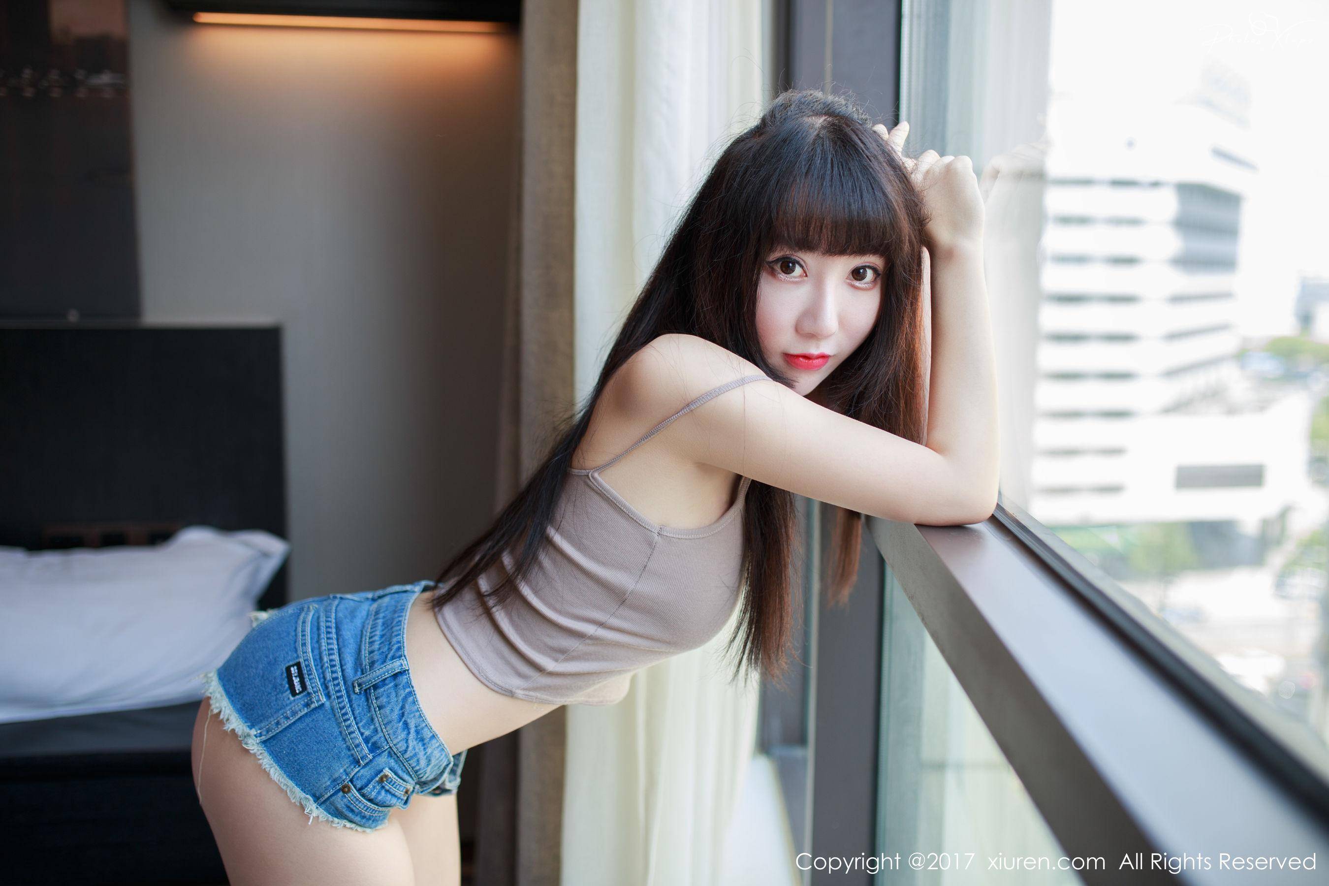 A young Asian woman with long black hair poses by a window in a cute outfit.