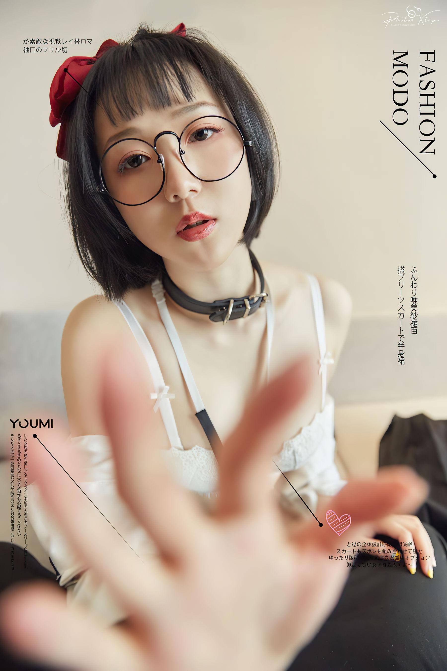 A fashion model with round glasses and a red bow in her hair. She is wearing a white dress and a black collar. The photo is set against a neutral background.