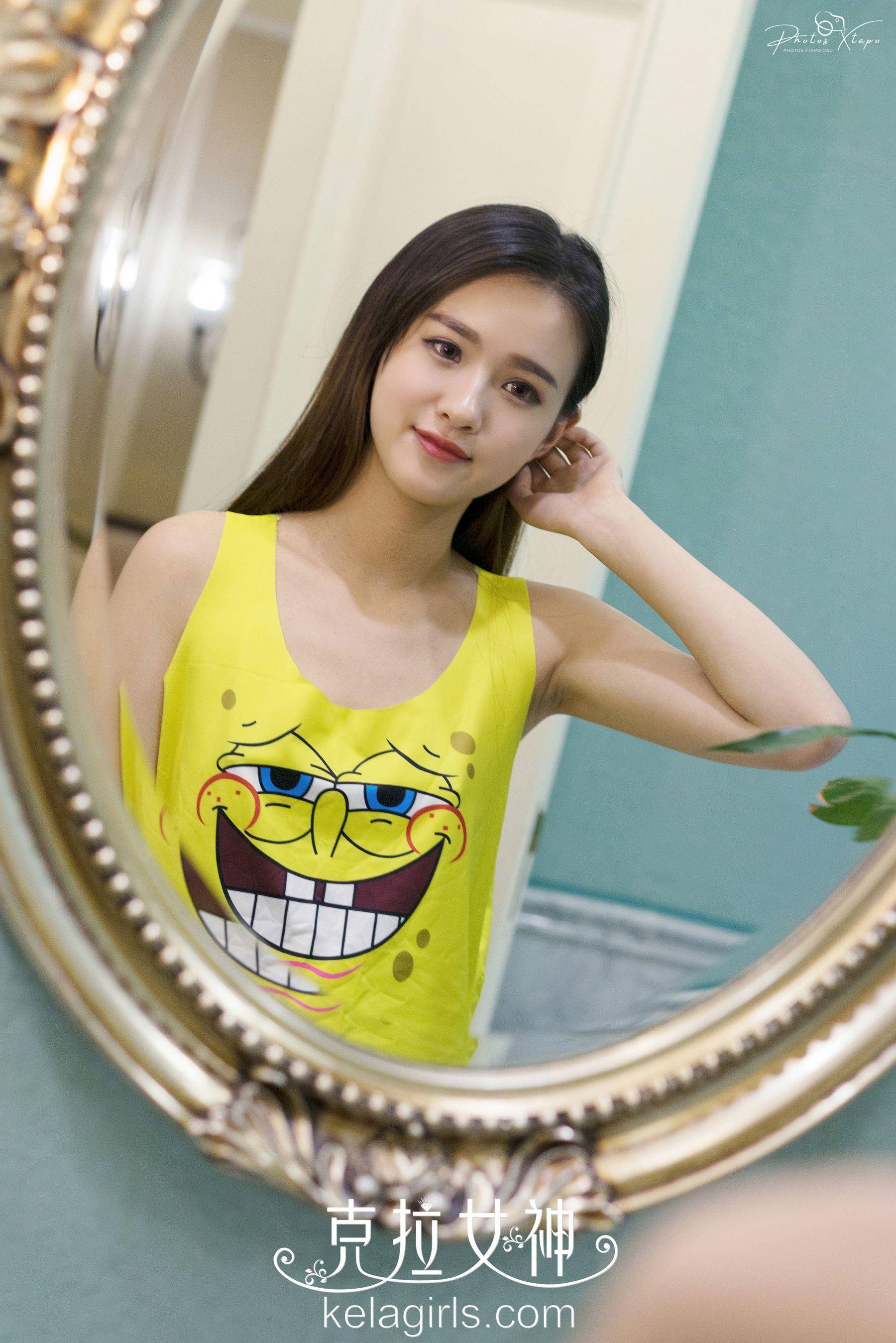 A young woman admires her reflection in a mirror while wearing a yellow tank top featuring SpongeBob Squarepants' face.