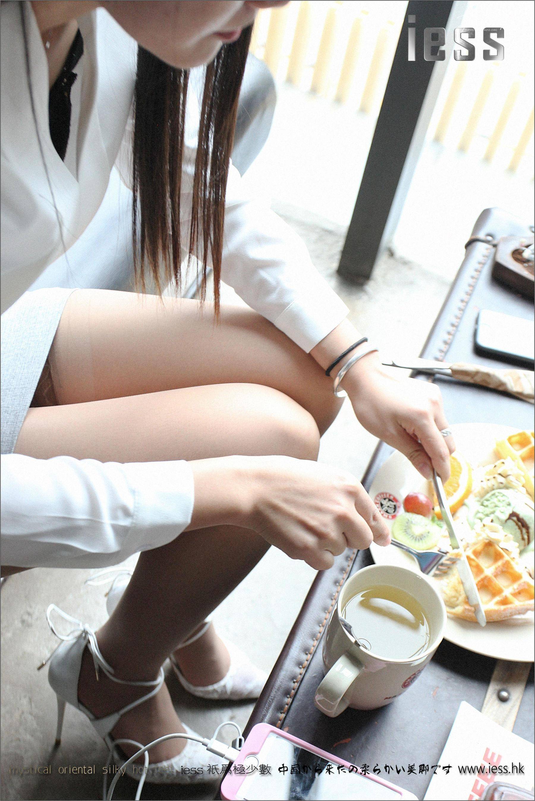A woman in a white blouse sits at a cafe table, enjoying a cup of tea and a waffle dessert.