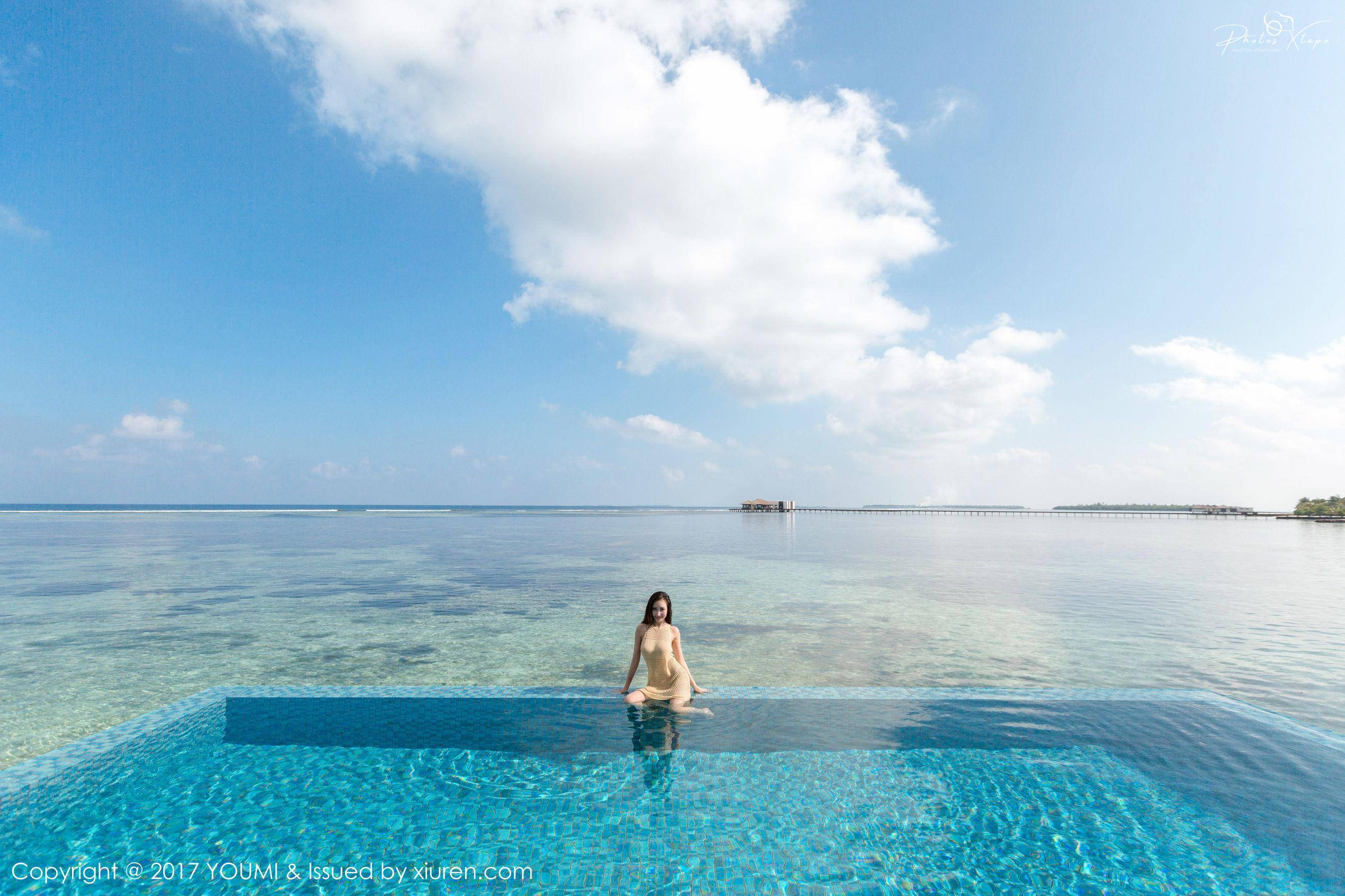 Woman relaxing by the infinity pool overlooking the turquoise ocean on a tropical island.